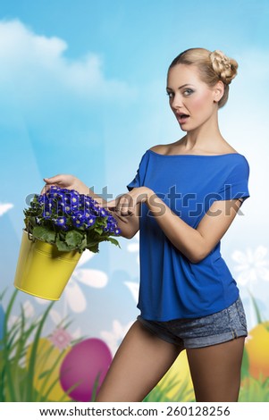 Blonde, young, pretty woman with bucket of blue flowers wearing t-shirt and jeans shorts. She has got funny hairstyle.