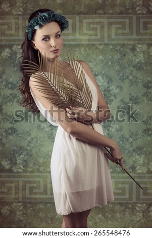 very pretty woman with long brown wavy hair posing in romantic spring portrait with flowers on head, white dress  and palm leafs in the hand