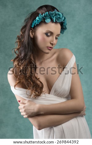 lovely sexy girl with long brown wavy hair posing in spring shoot with coloured make-up and flowers on the head, wearing sexy white dress