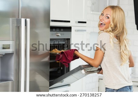 very expressive commercial woman , with happy face , cooking some food with oven , in her kitchen.