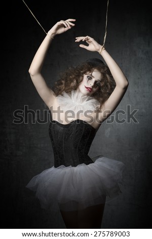 girl with gothic puppet dancer costume and sad clown make-up. She wearing vintage tutu and bowler hat. in marionette pose