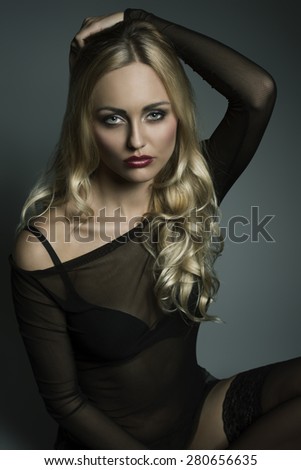 glamour blonde girl with long wavy hair and transparent dark underwear shirt, black bra and sexy stockings. Sitting and looking in camera with charming expression