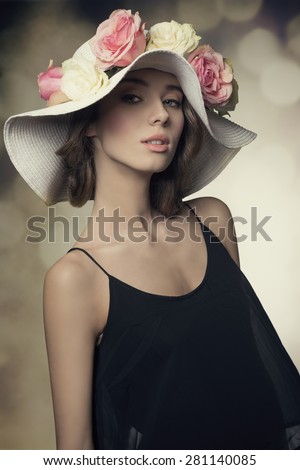 close-up portrait of elegant spring brunette woman with black dress and big hat with colorful flowers. Looking in camera, fashion pose