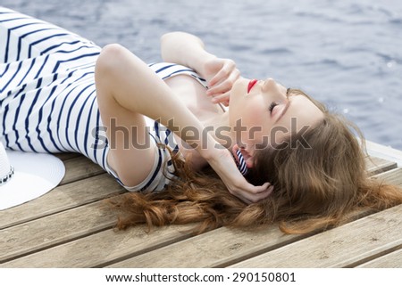 fashion woman lying relaxing on wood jetty near blue sea water in summertime. Wearing trendy summer striped dress.