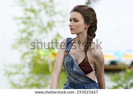 pretty woman with bikini and denim overall posing in outdoor summer portrait in the green nature with sea water on background
