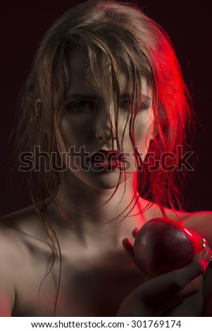 close-up portrait of sensual woman in red half-light with wet hair, red lipstick and apple in hand.