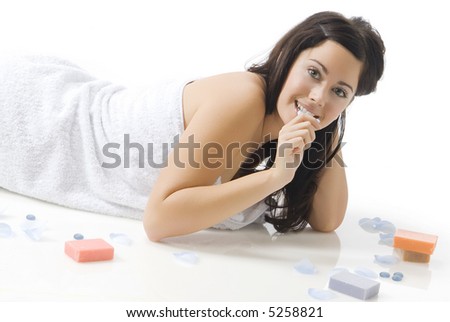 a cute young woman with dark hair and fair skin laying down on the floor near colored soap and petals
