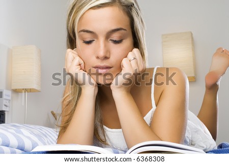 beautiful young woman with blond hair reading a book one evening in bed before to sleep