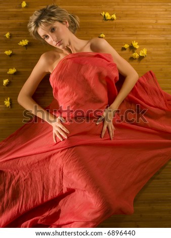 cute and attractive blond girl under a red soft fabric with flowers around