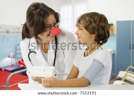 young and cute female doctor with a red nose taking blood pressure to a little boy