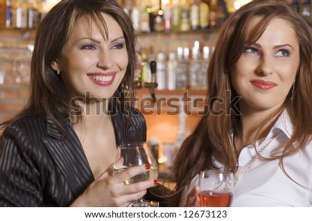 two young woman near a bar drinking and chatting each others