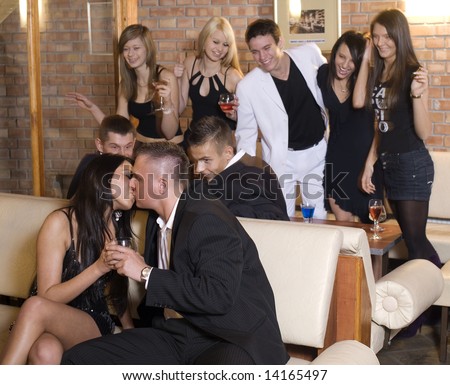 young couple kissing with friends behind laughing in moving focus on the couple