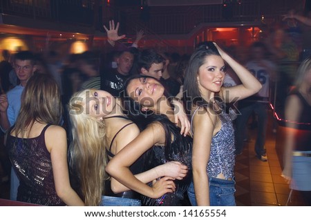 three girls dancing a night in disco with other people