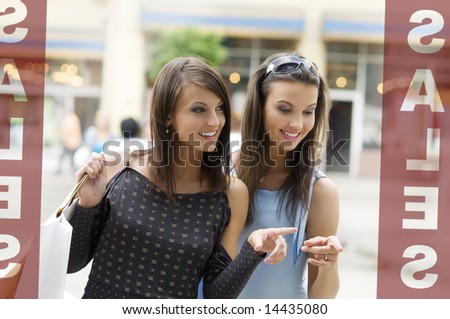two girls looking at a shop window during sales with a lot of interest