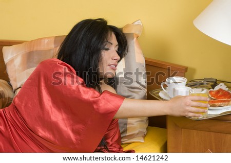 pretty woman laying down in bed taking a glass of orange juice from her breakfast