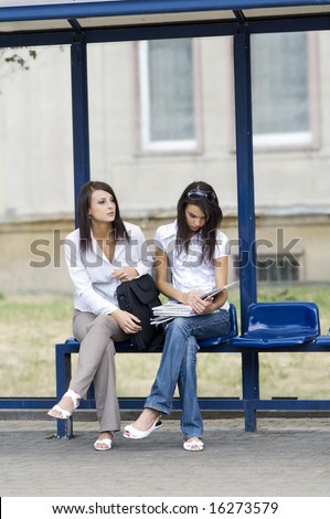two young and cute brunette waiting for a bus at the bus stop