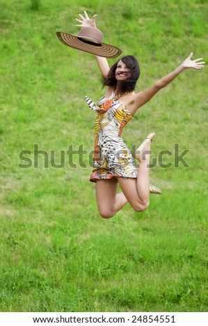 young athletic woman in colored dress and straw hat jumping in the field