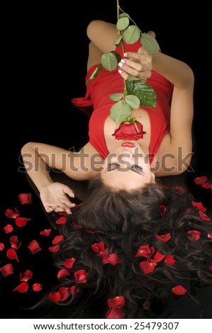 attractive woman in red elegant dress with petals between hair kissing a red rose