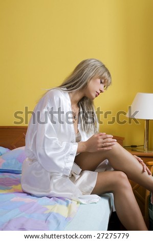 graceful blond woman in nightgown taking care of her leg before to sleep