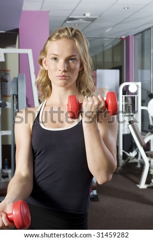 nice blond girl in a fitness club making exercise at mirror with dumb-bell
