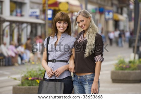two young beautiful girls standing in a street looking and smiling