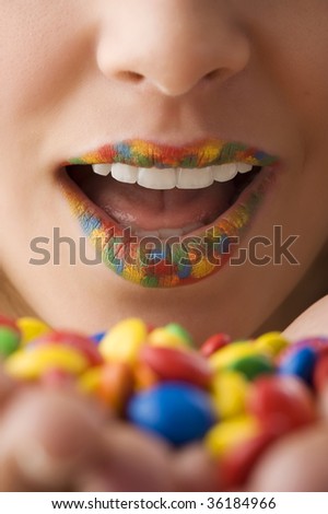close up on woman mouth with colored lips an color candy in hand