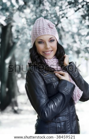 nice girl in winter dress with leather jacket and pink scarf and hat in a park with snow