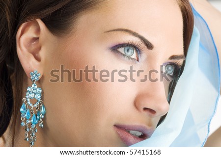 close up portrait of a pretty brunette with blue-sky earring playing to hide her face with a summer headscarf