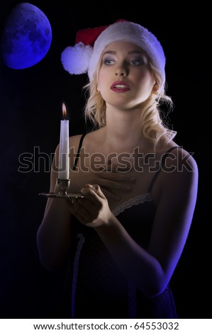 cute and attractive young woman with nightgown ant a christmas hat looking in the dark with a candle