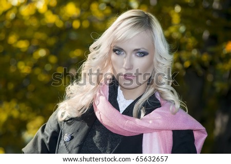 fashion portrait of young blond woman with hairstyle in winter dress with black coat and pink scarf outdoor in park