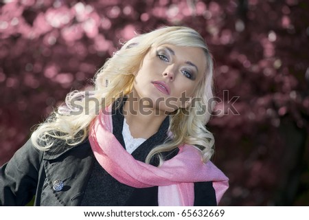 young blond woman with hairstyle wearing coat and scarf in a pink portrait outdoor