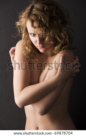 sexy young woman with naked shoulder and curly hair on black background looking very angry in camera