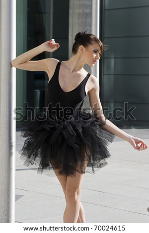 beautiful young ballet dancer in black tutu dancing outside near a modern building