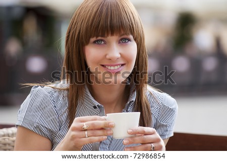 beautiful young woman sitting alone in a cafe outdoor and drinking a cup of tea looking in camera
