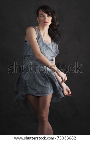 portrait of trendy young woman in elegant blue dress posing against black background