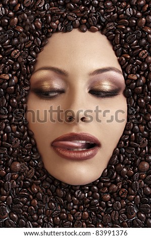 close up portrait of a girl\'s face immersed in coffee beans sticking her tongue out