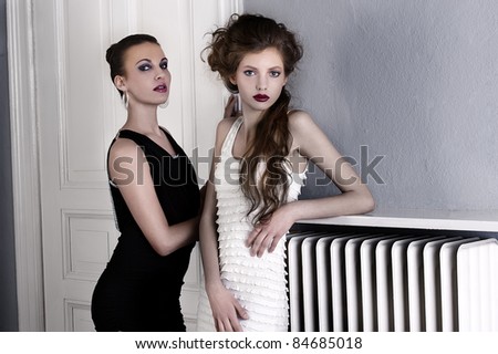 two beautiful women with hair style and elegant dress posing indoor near an old fashion door