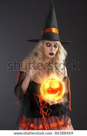 close up of a very sensual cute blond witch in orange and black dress with hat fortune telling with crystall ball