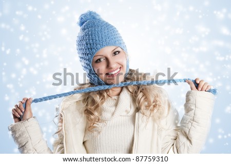 winter shot of a young pretty woman wearing a light blue hat and white sweater and scarf over white, in this shoot se\'s making a node with the pigtails of the hat.
