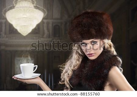 elegant fashion shot of a long haired blonde holding a hot cup of tea and wearing a fur stole and a huge brown fur hat