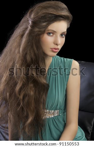 young elegant woman sitting on a black sofa with hair style and wearing a green dress looking in camera