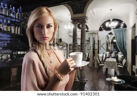 sensual blond girl with hair style drinking a cup of tea in elegant pink dress over dark fashion background