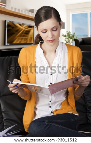 young girl student sitting on a sofa and reading a book, she takes a book with both hands and watches that.