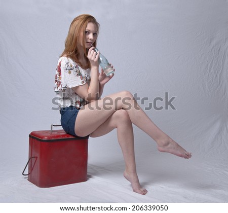 Model drinking soda while sitting on retro cooler.