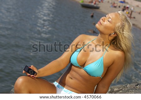 Young beautiful sexy tanned blond woman in hat and bikini laying on sea beach