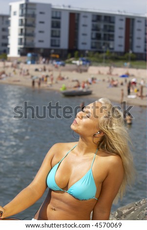 Young beautiful sexy tanned blond woman in hat and bikini laying on sea beach