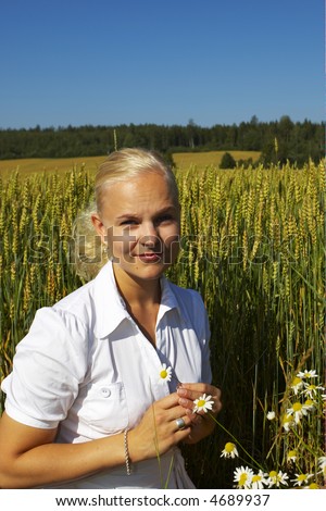 Dreamy girl wearing flowered blouse and white skirt standing in wheat cornfield touching delicately corn ears with her palms