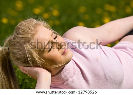 Woman lying in field of dandelions with face turned to sun