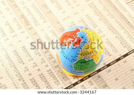 A globe sitting on a business newspaper showing stocks and share quotes