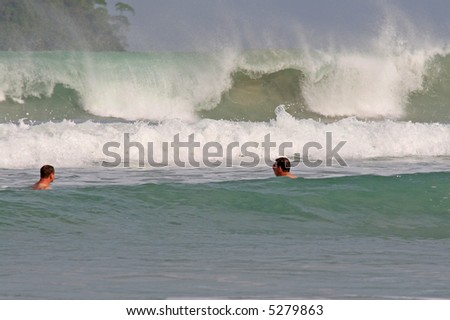 Tourists play in the water as large waves crash on a beach in Phuket, Thailand